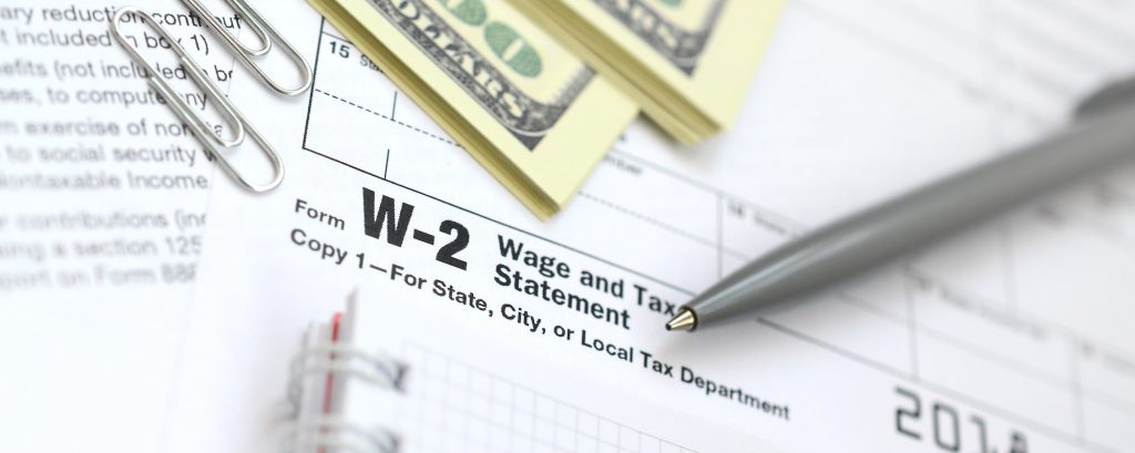 The pen, notebook and dollar bills is lies on the tax form W-2 Wage and Tax Statement