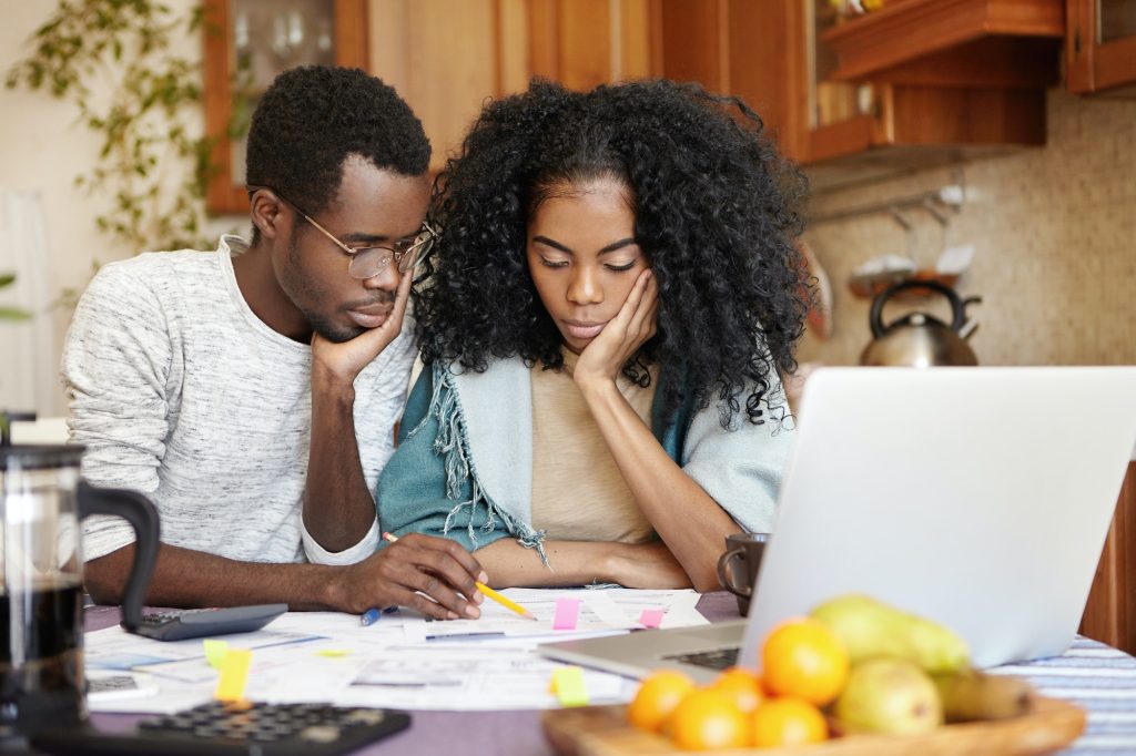 Upset young African-American couple feeling unhappy because they can't afford buying new car, facing